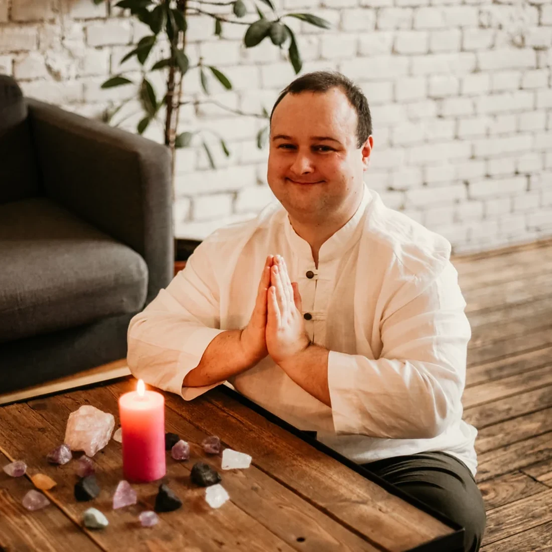 Martin Ospalík se sepjatýma rukama v namaste u dřevěného stolu se zapálenou svíčkou a polodrahokamy – kurzy Reiki od prvního stupně po velmistrovské stupně