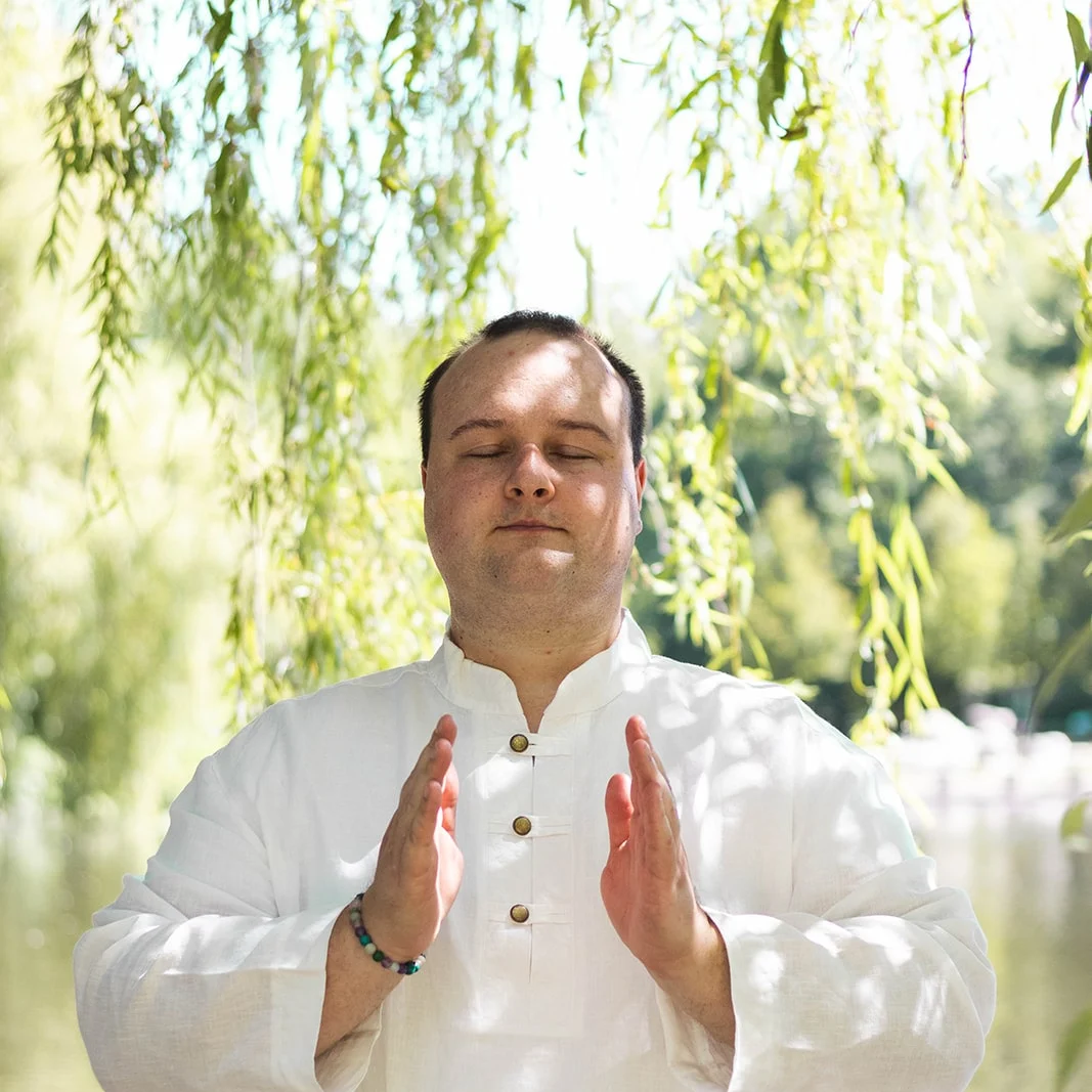 Martin Ospalík medituje pod vrbou u vody se zavřenýma očima a rukama před hrudí – Meditační akademie